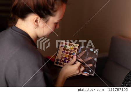 Woman holds makeup palette, choosing colors with focused expression. 131767195