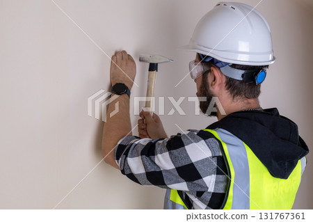 A construction worker is hammering a nail into a wall 131767361