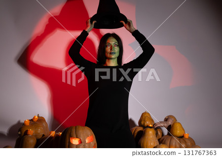 The woman is holding a witch hat above her head near with pumpkins 131767363