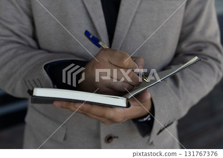 a person holding an open notebook and a pen, and the person's hand  131767376