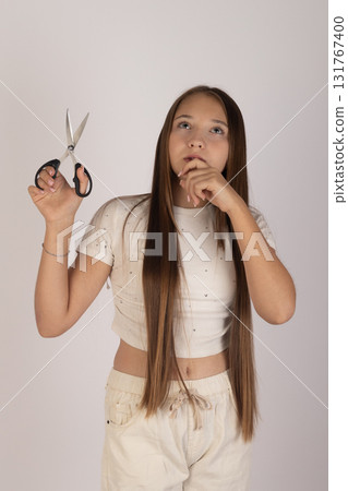 Girl is holding a scissors and appears to be contemplating cutting her long hair Girl is holding a scissors and appears to be contemplating cutting her long hair 131767400