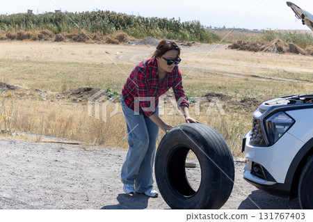 Woman putting a tire on a car in a mechanic shop with tools scattered around  131767403