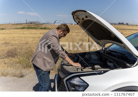 A man is looking under the open hood of a broken-down car 131767407