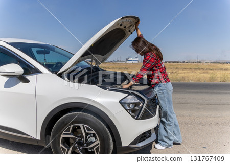 Woman inspecting car hood, puzzled expression Woman inspecting car hood, puzzled expression 131767409