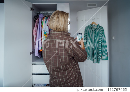 Middle aged Woman taking photo of shirt using smartphone for selling or donating her clothes. Decluttering , Sorting Clothes, And Cleaning Up wardrobe. Reuse, second-hand concept. Conscious consumer. Middle aged Woman taking photo of shirt using smartphone for selling or donating her clothes. Decluttering , Sorting Clothes, And Cleaning Up wardrobe. Reuse, second-hand concept. Conscious consumer. 131767465