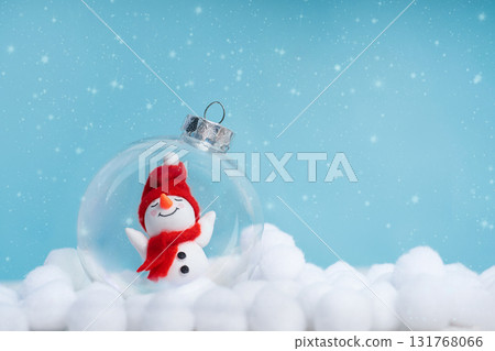 Cute snowman inside a glass ornament among artificial snowdrifts on a blue bokeh background. Christmas background with copy space for greeting cards, banners and holiday promos. 131768066