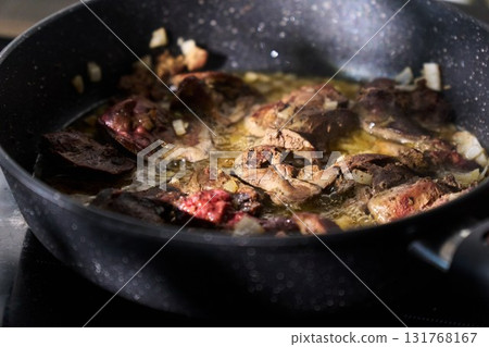 Cooking liver pieces in a frying pan with steam rising and kitchen appliances in the background Cooking liver pieces in a frying pan with steam rising and kitchen appliances in the background 131768167