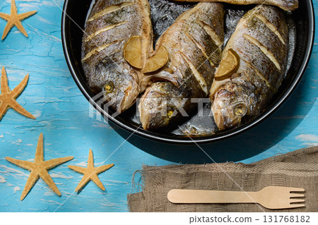 Freshly cooked dorado with lemon slices served on a rustic table with sea stars and coarse salt 131768182
