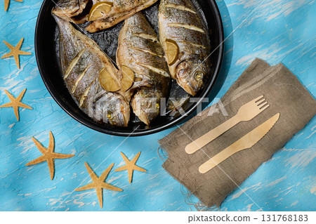 Fresh dorado fish arranged on a serving plate with lemon slices and sea salt on a bright blue background 131768183