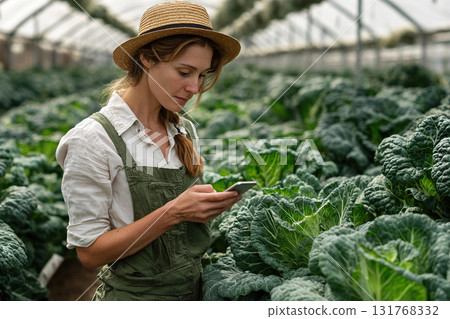 A woman, a small and medium-sized business owner, works in a fresh cabbage nursery. A female farmer uses a smartphone in a greenhouse. A budding entrepreneur. Fresh vegan food concept. 131768332