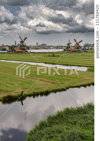 Scenic view of traditional Dutch windmills in Zaandam with changing skies, from calm daylight to approaching rain. Scenic view of traditional Dutch windmills in Zaandam with changing skies, from calm daylight to approaching rain. 131768420