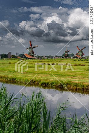 Scenic view of traditional Dutch windmills in Zaandam with changing skies, from calm daylight to approaching rain. 131768424