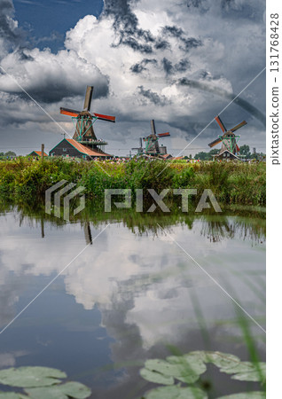 Scenic view of traditional Dutch windmills in Zaandam with changing skies, from calm daylight to approaching rain. 131768428