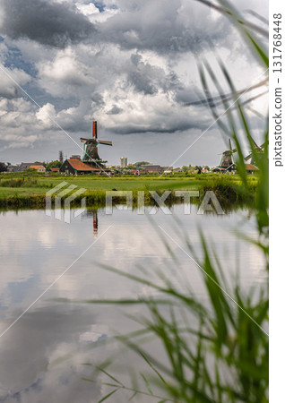 Scenic view of traditional Dutch windmills in Zaandam with changing skies, from calm daylight to approaching rain. 131768448