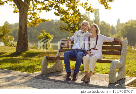 Beautiful stylish elderly couple in love is sitting on bench in city park on warm summer evening. Beautiful stylish elderly couple in love is sitting on bench in city park on warm summer evening. 131768707