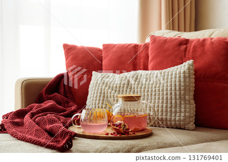 Glass Teapot and Teacup with Pomegranate Drink with Ginger and Citrus on Cozy Sofa with Autumn Decor 131769401