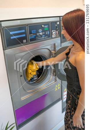 Young Man Taking Yellow Clothes Out of Washing Machine 131769695