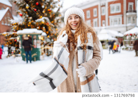 Young happy woman in a winter coat and scarf walks along a snowy city street. Concept of style. 131769798