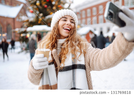 Young tourist uses a smartphone while walking through a Christmas market. 131769818