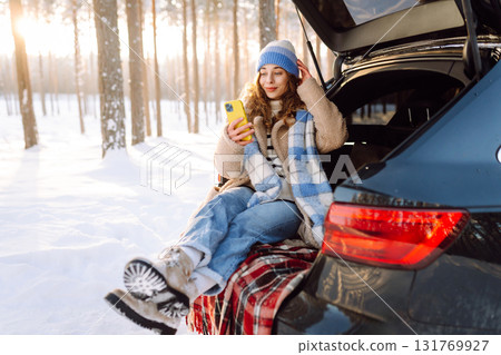 Happy Woman sitting in trunk, using phone. Snowy weather. Concept of adventure, travel by car. 131769927