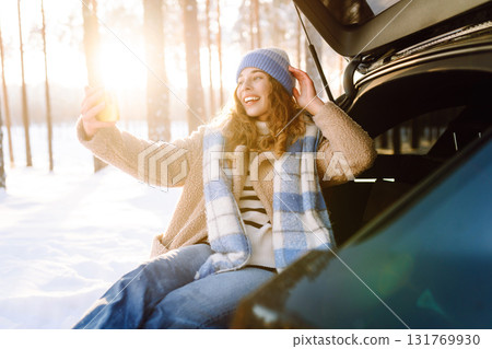 Selfie time. Young Woman sitting in trunk of car and taking selfie in winter forest. Rest, blogging. Selfie time. Young Woman sitting in trunk of car and taking selfie in winter forest. Rest, blogging. 131769930