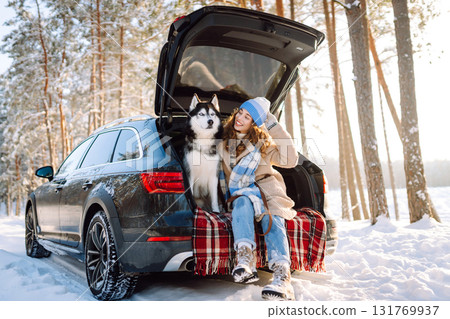 Woman with husky dog have picnic in car trunk near pine forest, traveling by car. Travel concept. Woman with husky dog have picnic in car trunk near pine forest, traveling by car. Travel concept. 131769937