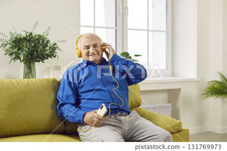 Smiling senior man in headphones listening to podcasts or music using phone 131769973