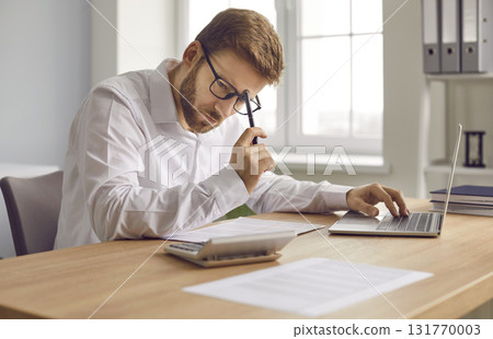 Financial accountant sitting at his office desk, calculating something, and thinking Financial accountant sitting at his office desk, calculating something, and thinking 131770003