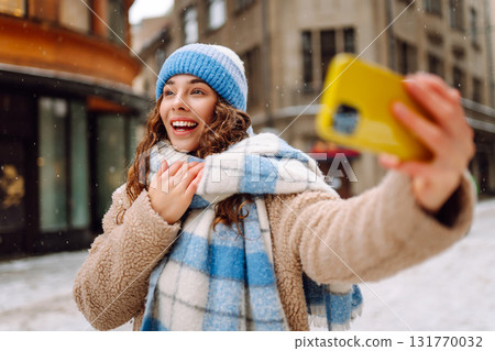 Young woman in winter time using phone outside the street. Selfie time. Holidays, rest, blogging. 131770032