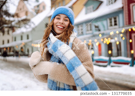 Happy woman in winter clothes walks on the street. Light all around. Winter holidays. 131770035