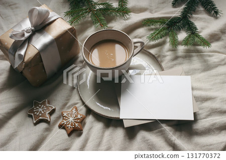 Winter still life. Cup of coffee, gingerbread cookies. Linen table cloth. Gift box with ribbon, fir tree branch. Christmas stationery. Blank greeting card, invitation mockup, envelope. Flatlay, top Winter still life. Cup of coffee, gingerbread cookies. Linen table cloth. Gift box with ribbon, fir tree branch. Christmas stationery. Blank greeting card, invitation mockup, envelope. Flatlay, top 131770372
