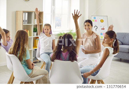 Group of school children girls sitting in a circle with psychologist and raising hands up. Group of school children girls sitting in a circle with psychologist and raising hands up. 131770654