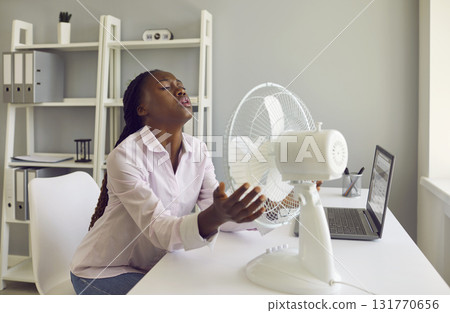 Woman office worker refreshes herself by electric fan at work in very hot summer 131770656