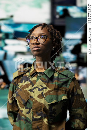 Female soldier wearing camouflage uniform in command center does surveillance and threat monitoring. Military officer oversees mission control with wall of live intelligence feed screens Female soldier wearing camouflage uniform in command center does surveillance and threat monitoring. Military officer oversees mission control with wall of live intelligence feed screens 131771207