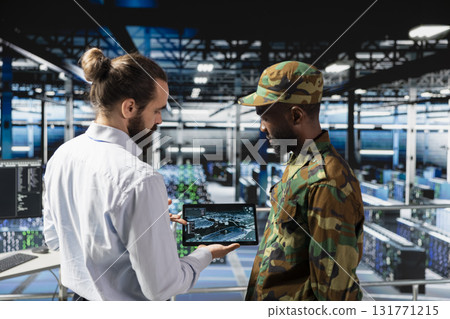 Military server room IT professionals using AI LLM tech on laptop to review network performance. Army operators managing hardware systems supporting armed forces mission for national security. 131771215