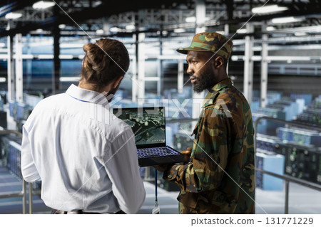 Military operator and IT expert in army data center using AI on laptop to manage autonomous defense systems. Soldier and programmer ensuring strategic threat detection tools for security. Military operator and IT expert in army data center using AI on laptop to manage autonomous defense systems. Soldier and programmer ensuring strategic threat detection tools for security. 131771229
