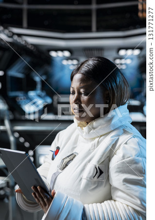 Female astronaut in spacecraft running diagnostics to confirm suit integrity using tablet. African american woman in orbital station testing gear during routine equipment check Female astronaut in spacecraft running diagnostics to confirm suit integrity using tablet. African american woman in orbital station testing gear during routine equipment check 131771277