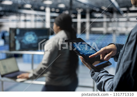 Close up of computer scientist in server hub using tablet to enhance AI model accuracy. Data center software developer using device to schedule maintenance for AI hardware rigs 131771310