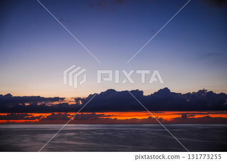 Early dawn over the calm Mediterranean Sea in Spain with dark clouds above the glowing orange horizon before sunrise. 131773255