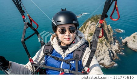 Asian woman taking selfie while paragliding over stunning turquoise ocean coastline with rocky cliffs and scenic aerial landscape view 131773610