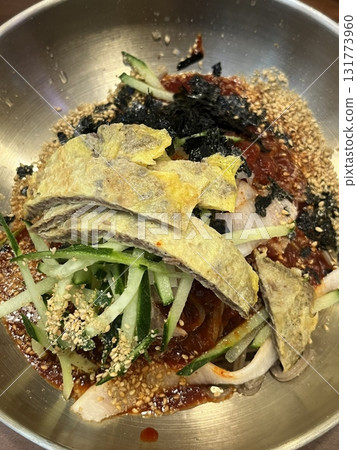 Naengmyeon, a refreshing Korean cold noodle dish served in an icy broth, topped with sliced vegetables, a boiled egg, and spicy sauce. Perfect for summer food photography and Korean cuisine projects. 131773960