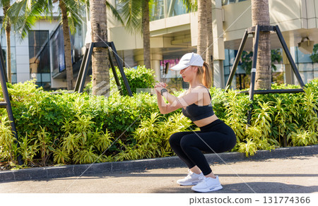 Sport woman performs outdoor workout, fit body does deep squat exercise, people enjoy urban sport, healthy active lifestyle includes stretch routine. Sport woman performs outdoor workout, fit body does deep squat exercise, people enjoy urban sport, healthy active lifestyle includes stretch routine. 131774366