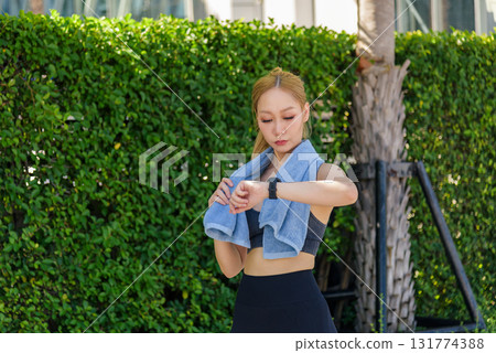 Sport woman checking smartwatch during outdoor exercise, fit athlete engaged in workout activity, preparing for next rigorous sport session in green natural surroundings. 131774388