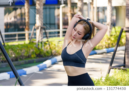 Sport woman exercises with headphones, performing outdoor workout, young fit woman stretches body, enjoying active healthy lifestyle with daily sport training. 131774430