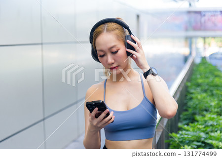 Exercise woman performs sport workout outdoor, adjusting headphones, checking phone and smartwatch for fitness tracking, people pursuing health and wellness through regular exercise. Exercise woman performs sport workout outdoor, adjusting headphones, checking phone and smartwatch for fitness tracking, people pursuing health and wellness through regular exercise. 131774499