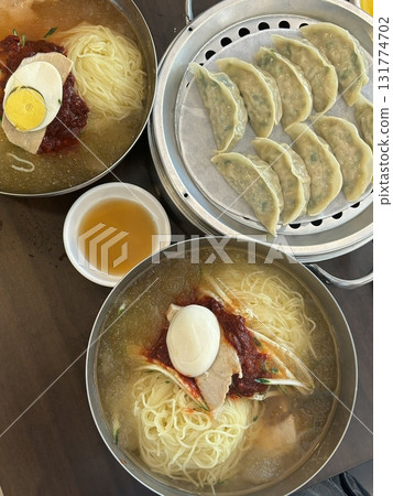 Chilled, chewy naengmyeon noodles in tangy broth paired with juicy, savory mandu dumplings, offering a perfect balance of refreshing coolness and hearty comfort in every delicious Korean bite. 131774702