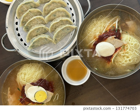Chilled, chewy naengmyeon noodles in tangy broth paired with juicy, savory mandu dumplings, offering a perfect balance of refreshing coolness and hearty comfort in every delicious Korean bite. 131774703