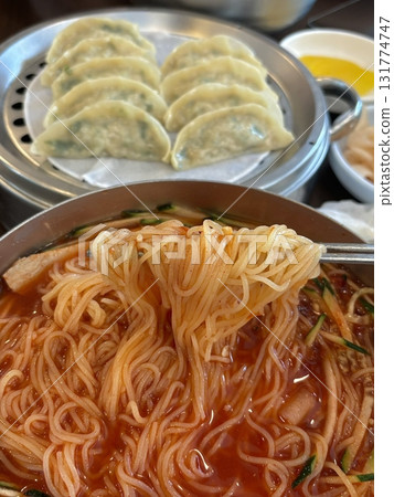 Chilled, chewy naengmyeon noodles in tangy broth paired with juicy, savory mandu dumplings, offering a perfect balance of refreshing coolness and hearty comfort in every delicious Korean bite. 131774747