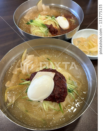 Naengmyeon, a refreshing Korean cold noodle dish served in an icy broth, topped with sliced vegetables, a boiled egg, and spicy sauce. Perfect for summer food photography and Korean cuisine projects. 131775155