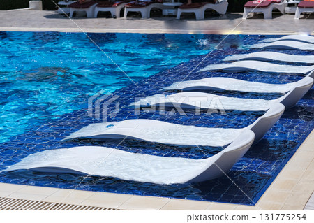 A pool with a row of white lounge chairs on the side 131775254